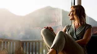 a woman sitting in a house, looking in the direction of mountains and thinking about the new Fronius warranty