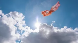 A piece of pink, translucent fabric floating in the sky against bright sunlight and white clouds